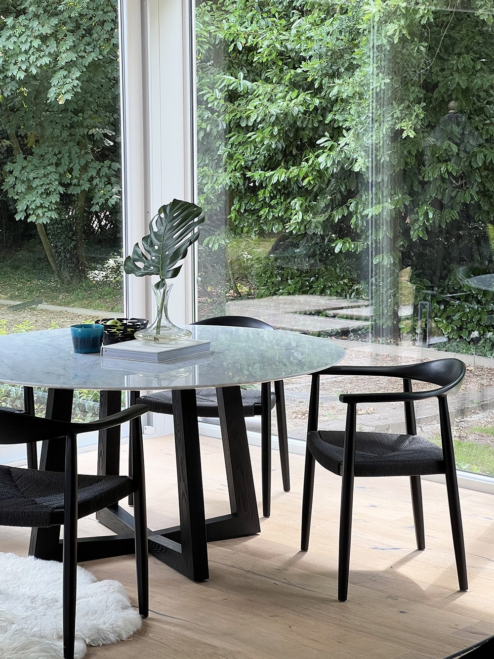 Betover je interieur met onze ronde "Nox" tafel, voorzien van een luxueus Bianco Carrara marmeren blad met een diameter van 150cm en ondersteund door een prachtig gekruist houten onderstel